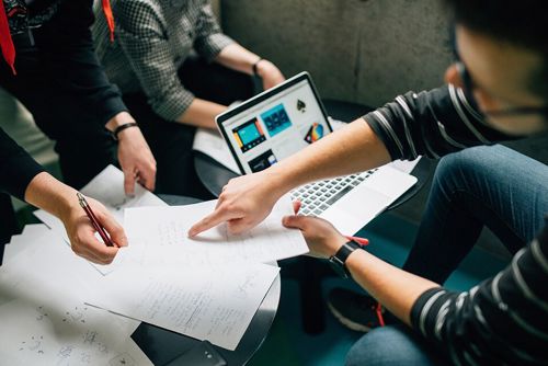 Three students collaborate over several bits of paper and an open laptop