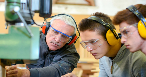 A tutor teaches two students to use a drill press