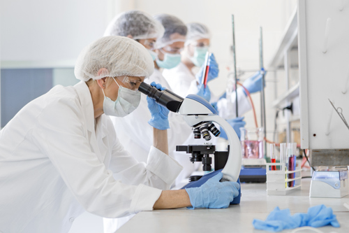 Four people in a clinical research setting, the nearest looking in a microscope