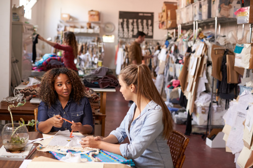 Two friends sit in a craft shop surrounded by crafting items