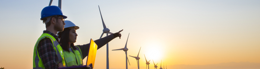 Apprentices standing in front of a wind farm with a laptop